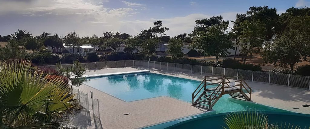 Une piscine extérieure avec des chaises longues sur le côté est entourée d'une clôture de sécurité et de végétation
