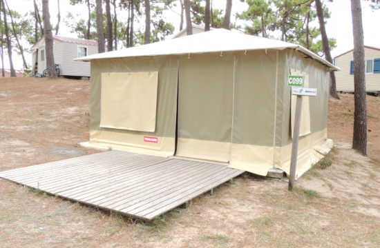 La tente de couleur beige est montée sur une plateforme en bois dans un environnement de terrain de camping avec un panneau indiquant "C099".