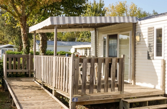 La terrasse en bois d'un mobile-home est équipée d'une balustrade et d'un auvent rayé, et porte le numéro 48.